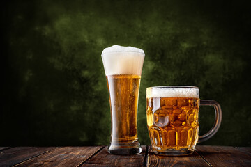Glass and mug of beer on dark green background and wooden table with copyspace