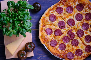 Classic pepperoni pizza with tomato sauce, cheese and salami sausage on a black wooden background.