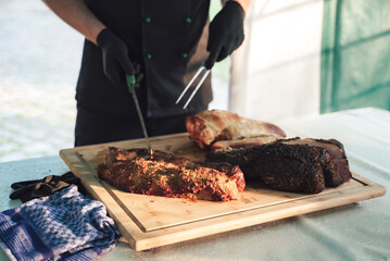 Several pieces of roasted beef meat laying on wooden board. Man standing and offering choice of piece. Celebration, party, birthday or wedding concept