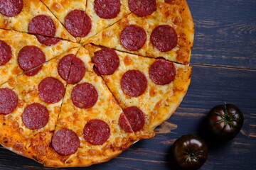 Classic pepperoni pizza with tomato sauce, cheese and salami sausage on a black wooden background.