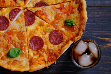 Pizza and cola with ice and lemon. Pepperoni and Margarita. Two pizzas together and a cola on a wooden table.