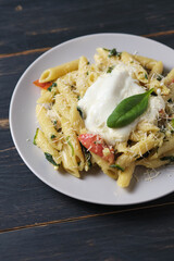 Pasta with tomatoes, spinach, parmesan and bolognese sauce. Serving dish in a plate on a wooden table.