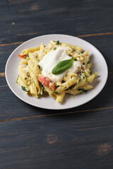 Pasta with tomatoes, spinach, parmesan and bolognese sauce. Serving dish in a plate on a wooden table.