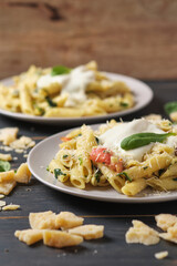 Two portions of pasta with tomatoes, spinach, parmesan and bolognese sauce. Dish in a plate on a wooden table.
