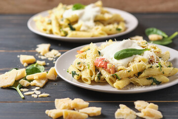 Two portions of pasta with tomatoes, spinach, parmesan and bolognese sauce. Dish in a plate on a wooden table.