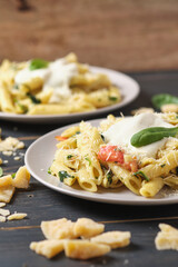 Two portions of pasta with tomatoes, spinach, parmesan and bolognese sauce. Dish in a plate on a wooden table.