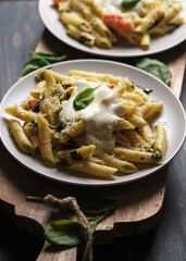Two portions of pasta with tomatoes, spinach, parmesan and bolognese sauce on a large kitchen wooden board. Dish in a plate on a wooden table.