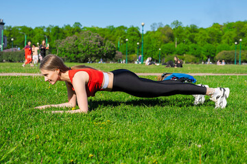 Girl performs an exercise plank in the park on the grass. Leads a healthy lifestyle. Keeps track of...