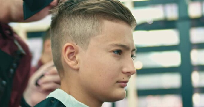 Serious Caucasian boy getting hairstyle in barbershop.