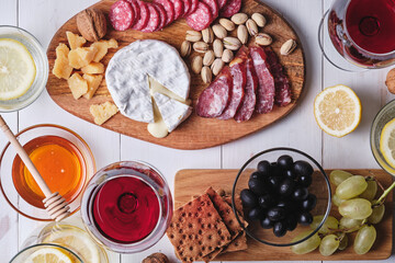 Delicious products for a romantic dinner. Cheese and sausage delicacies, nuts, fruits, olives, bread, grapes, wine and honey on an old white wooden table. Top view.