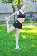 Girl in the park does a workout before a run. Stretches the muscles of the legs