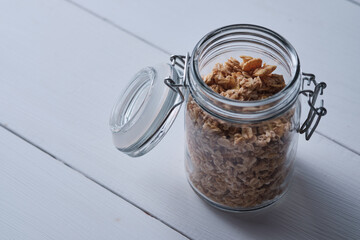 Jar with granola on a white wooden table.