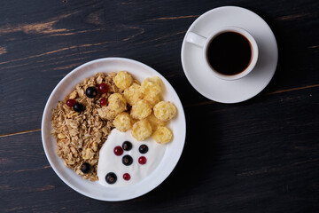 Muesli with yogurt and fresh berries in a plate. Breakfast on a dark wooden table.