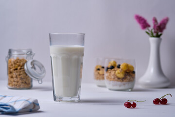 A glass of milk and granola with yogurt and fresh berries. Breakfast on a white wooden table.