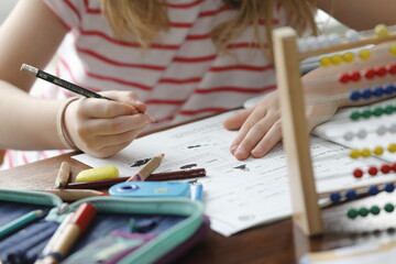 Kleines Mädchen macht in Heimschule Mathe Hausaufgaben zuhause mit Mäppchen, Rechenschieber, Stiften.