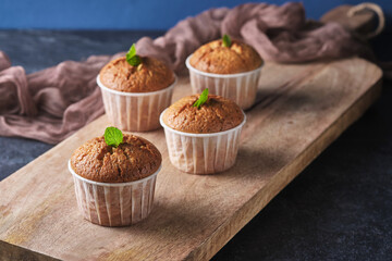 Lemon muffins with poppy seeds, decorated with mint, on a wooden board. Background color classic blue.
