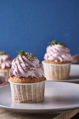 Festive cupcakes with pink cream on a plate. The dessert is decorated with mint leaves and chocolate chips. Background color classic blue.