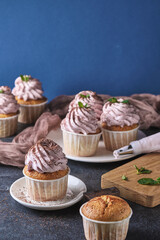 The process of making holiday cupcakes with pink cream. The dessert is decorated with mint leaves and chocolate chips. Background color classic blue.