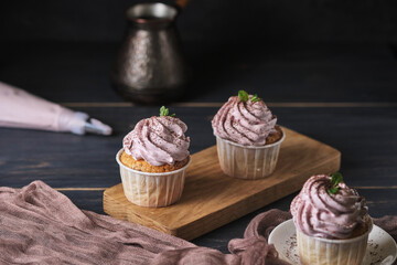 Holiday cupcakes with pink cream. The dessert is decorated with mint leaves and chocolate chips. Cupcakes and coffee. Background color classic blue.