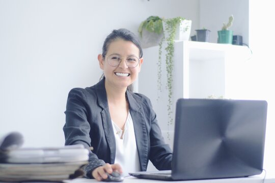 Joven mujer de negocios sonr&iacute;e mientras trabaja en la computadora port&aacute;til. Mujer trabajando