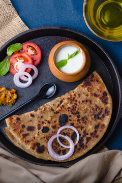 Aloo Paratha / Indian Potato Stuffed Wheat Bread served with Curd & Pickle, Tomato & Onion. Top View on a Dark Moody Background. Traditional North Indian or Punjabi Breakfast. For Food Blog or Menus.