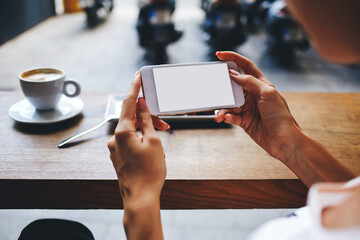 young female reading news via cell telephone while sitting in coffee shop