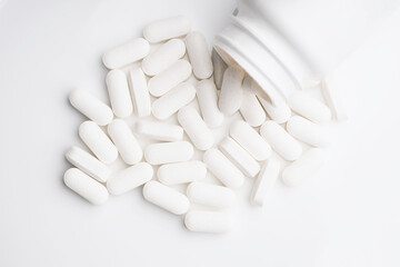 Medication bottle and white pills spilled on white background.