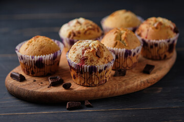 Cupcakes with berries and chocolate on a wooden board.