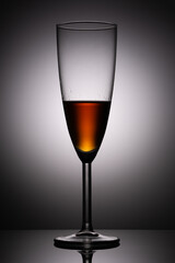 A glass of cognac on the background of a light spot in the dark with a reflection in the glossy surface of the table. Product photography studio shot.