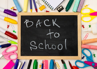 Back to school black chalk board on a white wooden background, color supplies. Top view. Copyspace. Education concept.