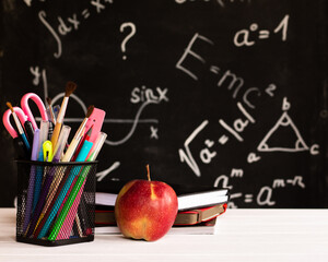 Coloured school supplies, apple, books on white wood contertop on chalkboard background with formulas. Education concept