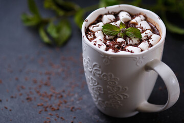 A mug of mint hot chocolate with marshmallows on a dark background. White mug of hot drink close-up.