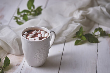 Mug of mint hot chocolate with marshmallows on a white wooden table. Autumn evening: books, chocolate and a hot warming drink.