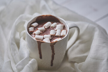 Mug of hot chocolate with marshmallows on a light textile background. White mug of hot drink close-up.