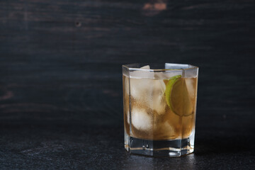 Glass with an alcoholic cocktail on a table in a bar. Whiskey with ice garnished with lime.