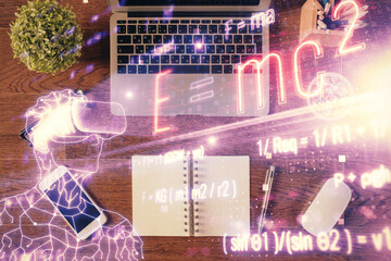 Physics and math theme hologram with formula drawings over computer on the desktop background. Top...