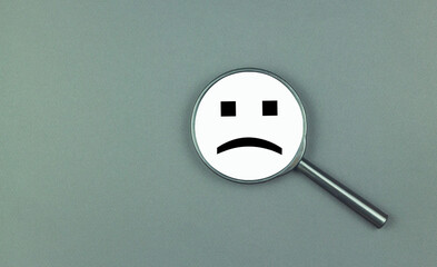 A negative smile is depicted on a magnifying glass. The concept of depression, ill health, failure, frustration, bad luck, anger and defeat.
