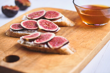 Bruschettas with figs, soft cheese and honey on a wooden board.