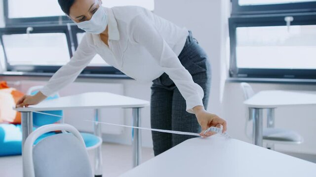 Teacher back at school after covid-19 quarantine and lockdown, measuring distance of desks.