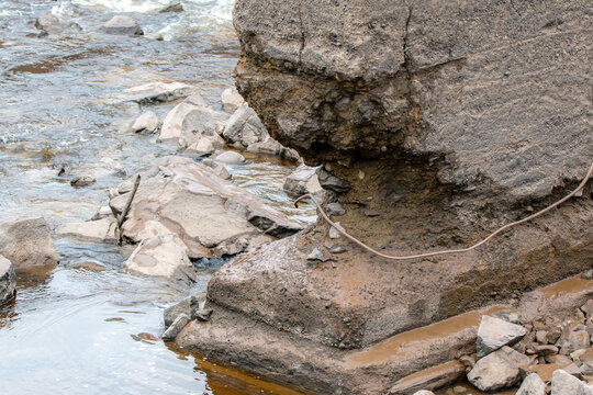 The bottom of an eroded concrete bridge support in a river. The support is heavily eroded at the bottom.