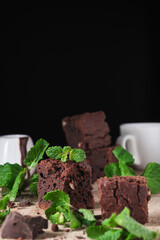 Chocolate brownie with nuts and mint. Sweet and tasty dessert decorated with mint, closeup on a wooden table. Soft focus.