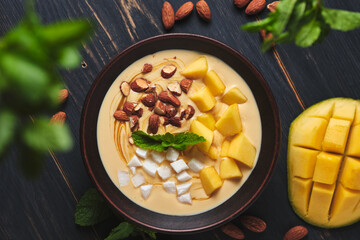 Tropical smoothie bowl with banana, mango, coconut and nuts. Refreshing dessert with mint on an old wooden table. Diet and delicious breakfast for the whole family.