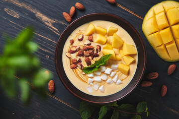 Tropical smoothie bowl with banana, mango, coconut and nuts. Refreshing dessert with mint on an old wooden table. Diet and delicious breakfast for the whole family.