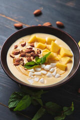 Tropical smoothie bowl with banana, mango, coconut and nuts. Refreshing dessert with mint on an old wooden table. Diet and delicious breakfast for the whole family.