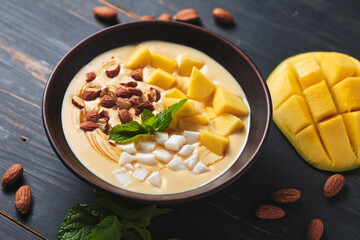 Tropical smoothie bowl with banana, mango, coconut and nuts. Refreshing dessert with mint on an old wooden table. Diet and delicious breakfast for the whole family.