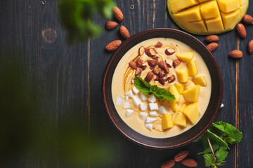 Tropical smoothie bowl with banana, mango, coconut and nuts. Refreshing dessert with mint on an old wooden table. Diet and delicious breakfast for the whole family.