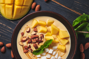 Tropical smoothie bowl with banana, mango, coconut and nuts. Refreshing dessert with mint on an old wooden table. Diet and delicious breakfast for the whole family.
