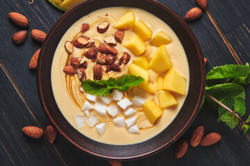 Tropical smoothie bowl with banana, mango, coconut and nuts. Refreshing dessert with mint on an old wooden table. Diet and delicious breakfast for the whole family.