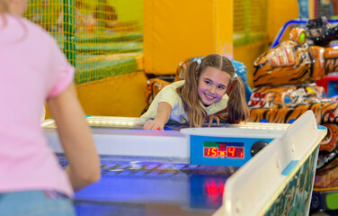 Lovely girl playing air hockey game with her mum at kids amusement center