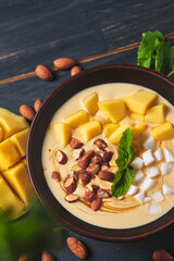Tropical smoothie bowl with banana, mango, coconut and nuts. Refreshing dessert with mint on an old wooden table. Diet and delicious breakfast for the whole family.